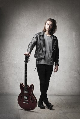 Waiting for his time in the light, the young guitarist stands with his instrument.